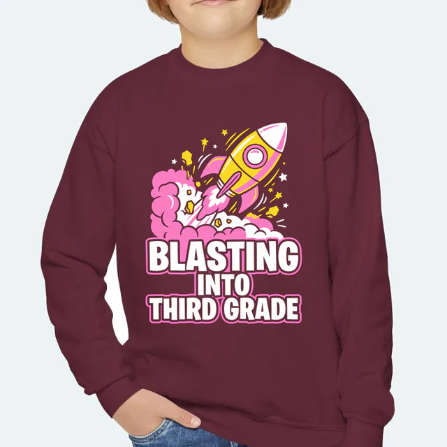 A rocket lifting off in smoke and stars, BLASTING INTO THIRD GRADE, on a maroon youth crewneck