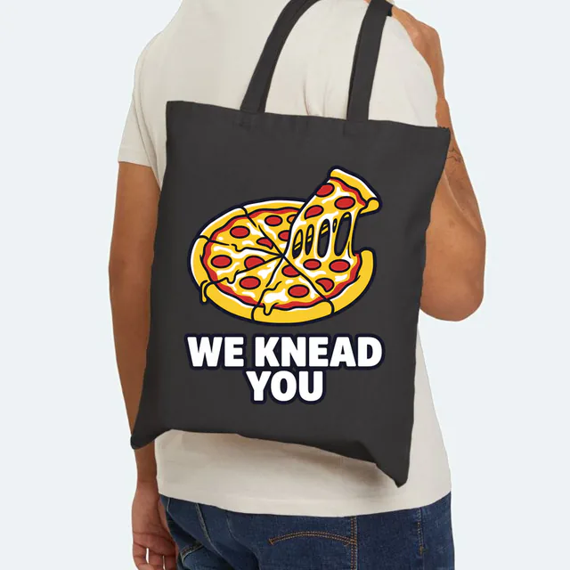 A pizza slice pulling away with stretchy cheese, WE KNEAD YOU, on a black canvas tote