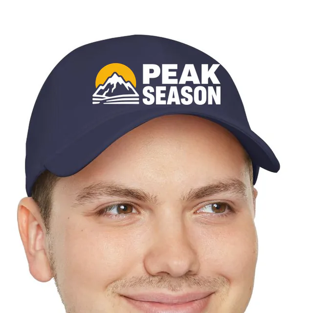 A mountain peak and sun beside PEAK SEASON, on a navy dad hat