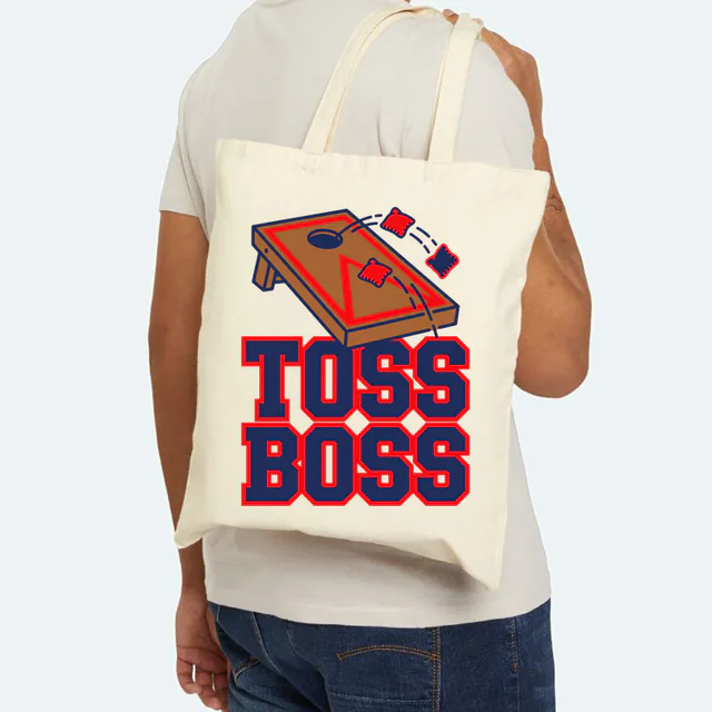Beanbags arcing toward the board, TOSS BOSS, on a natural canvas tote