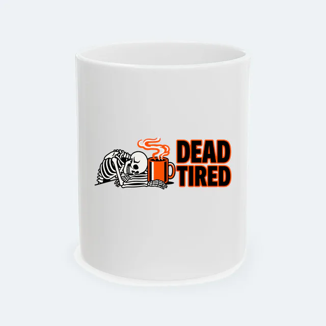A sleepy skeleton slumped over its coffee, DEAD TIRED, on a white ceramic mug