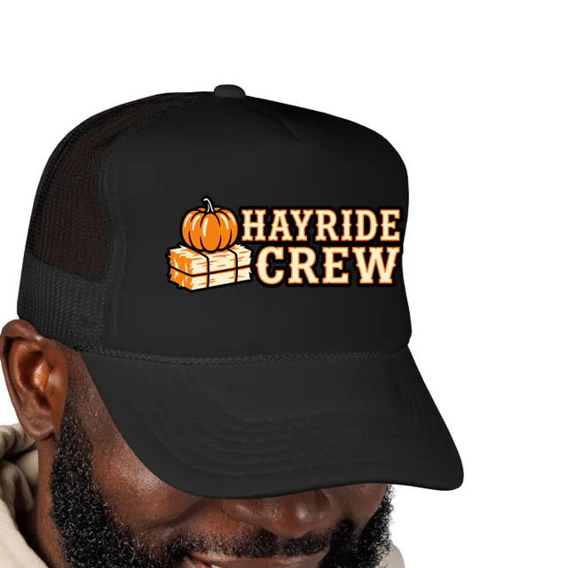 A pumpkin on a hay bale beside HAYRIDE CREW, on a black foam trucker hat