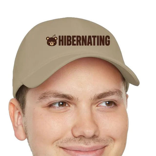 A sleeping bear face beside HIBERNATING, on a khaki dad hat