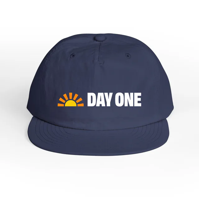 A small sunrise beside DAY ONE, on a cobalt surf cap