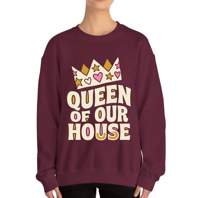 A crooked paper crown over QUEEN OF OUR HOUSE, on a maroon adult crewneck