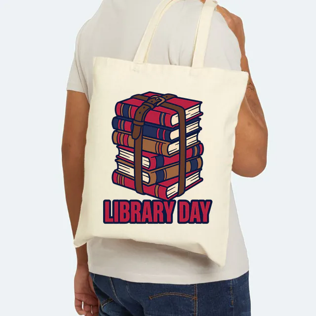 A strapped stack of library books over LIBRARY DAY, on a natural canvas tote