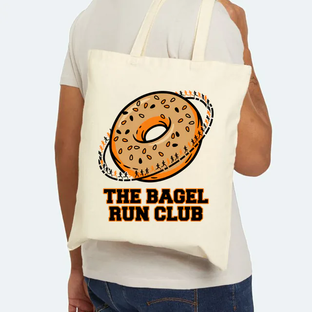 Tiny runners circling a giant bagel, THE BAGEL RUN CLUB, on a natural canvas tote