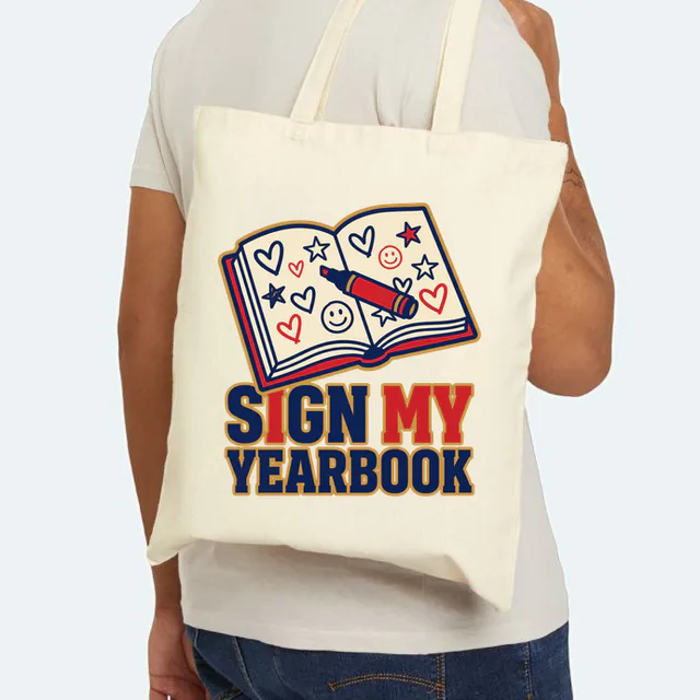 An open yearbook covered in doodles, SIGN MY YEARBOOK, on a natural canvas tote