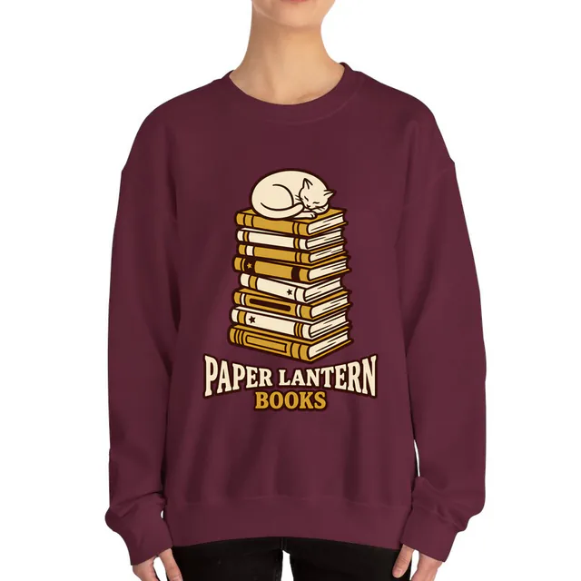 A cat asleep on a stack of books, PAPER LANTERN BOOKS, on a maroon adult crewneck