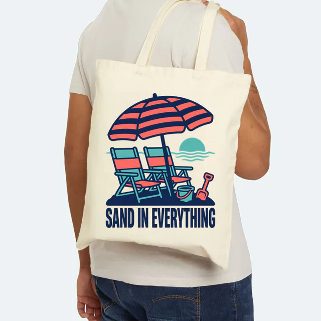 A beach umbrella over two chairs, SAND IN EVERYTHING, on a natural canvas tote