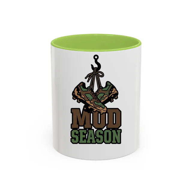 Muddy cleats hanging by their laces, MUD SEASON, on a light green accent mug