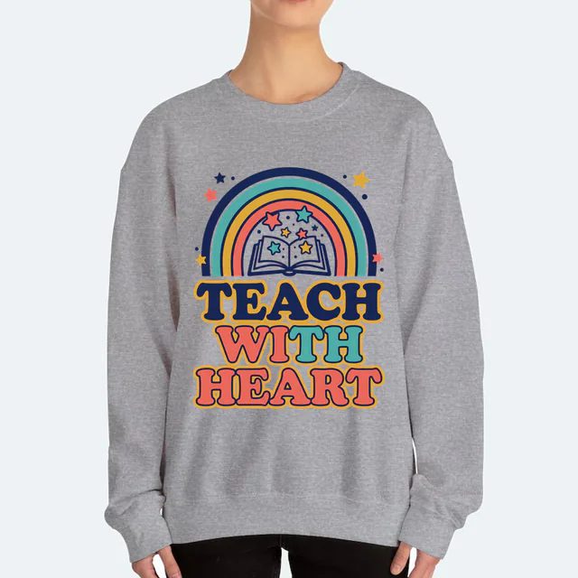 A retro rainbow over an open book, TEACH WITH HEART, on a sport gray adult crewneck