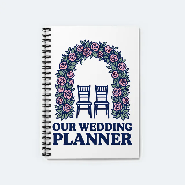 A floral arch over two chairs, OUR WEDDING PLANNER, on a white spiral notebook