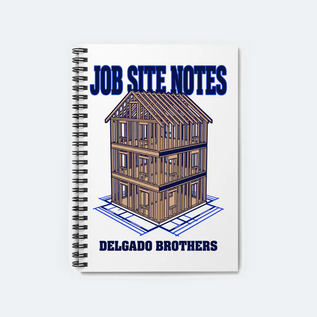 A wood house frame on a blueprint grid, JOB SITE NOTES, on a white spiral notebook
