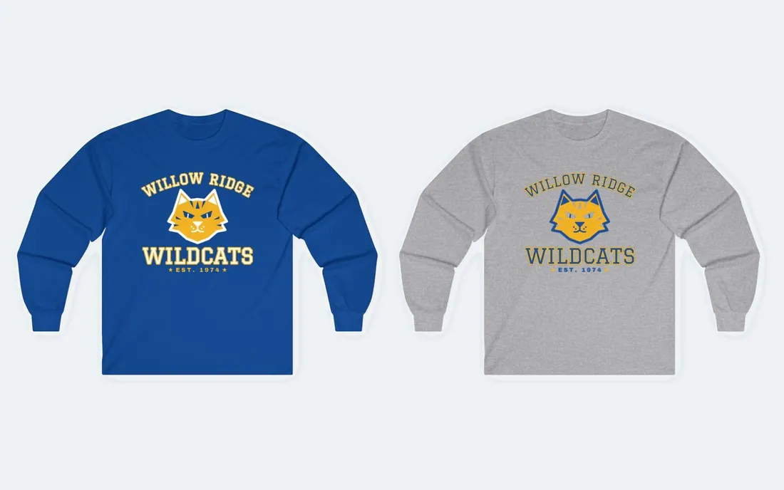 Two long sleeve school spirit shirts laid flat, a royal blue one and a grey one, each printed with an arched Willow Ridge name over a wildcat mascot and the word Wildcats